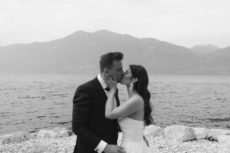 Hochzeitsfotograf Gardasee 27 Brautpaar küsst sich am Ufer des Gardasees vor den Bergen