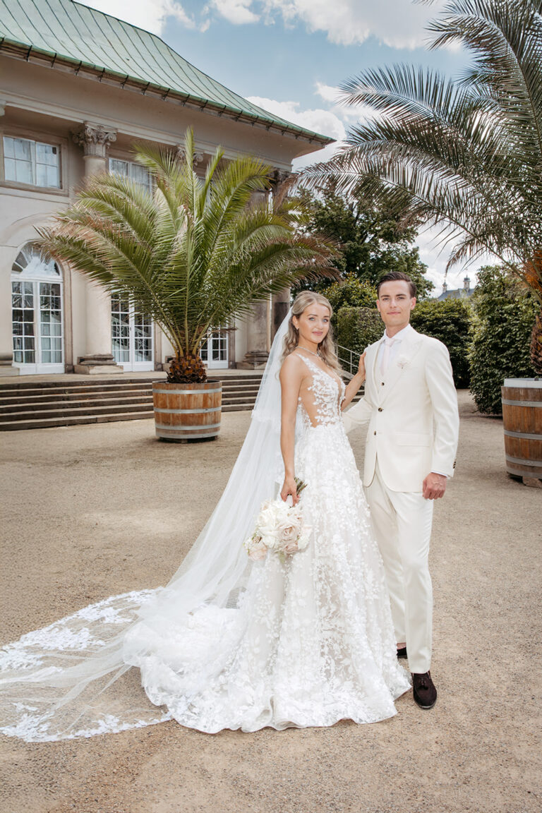 Elegantes Brautpaar in Weiß vor Palmenkulisse bei Hochzeitsreportage in Dresden.